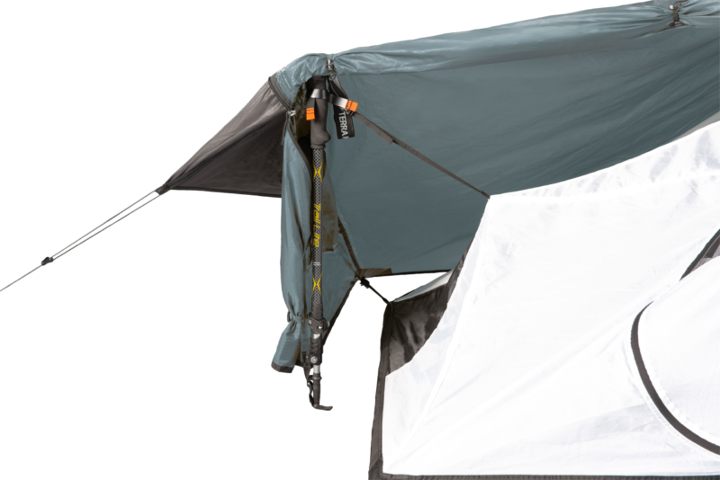 Close-up of a grey-blue tent awning secured by an adjustable trekking pole and orange strap clips, with a white tent wall and taut guy lines visible.