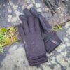 A pair of black waterproof gloves with textured grip patterns and water droplets lying on wet, lichen-covered rocks beside a small patch of grass.