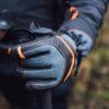 Zenith_Gloves_LS-9-scaled-2.jpg Close-up of a grey and black hiking glove with orange stitching and a wrist strap gripping a trekking pole against a blurred outdoor background.
