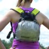 zoom_Laser_Ultra_5_Pack_1-1.jpg Rear view of a person with a ponytail wearing a purple running top and a small silver ultralight running backpack with bright yellow shoulder straps against a cloudy sky