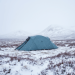 A blue tent set against a snowy landscape with mountains in the background, showcasing a winter camping scene in a remote area.