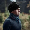 Contour Waterproof Eco Polyana Beanie Lifestyle Man wearing a black beanie and a blue scarf, standing outdoors in a natural setting, with trees in the background, showcasing active outdoor apparel suitable for cold weather.