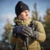 LIN-TERRANOVA-725970-221011-1134-RT Man wearing a warm jacket and gloves, holding trekking poles, standing outdoors in a forested area with a clear sky.