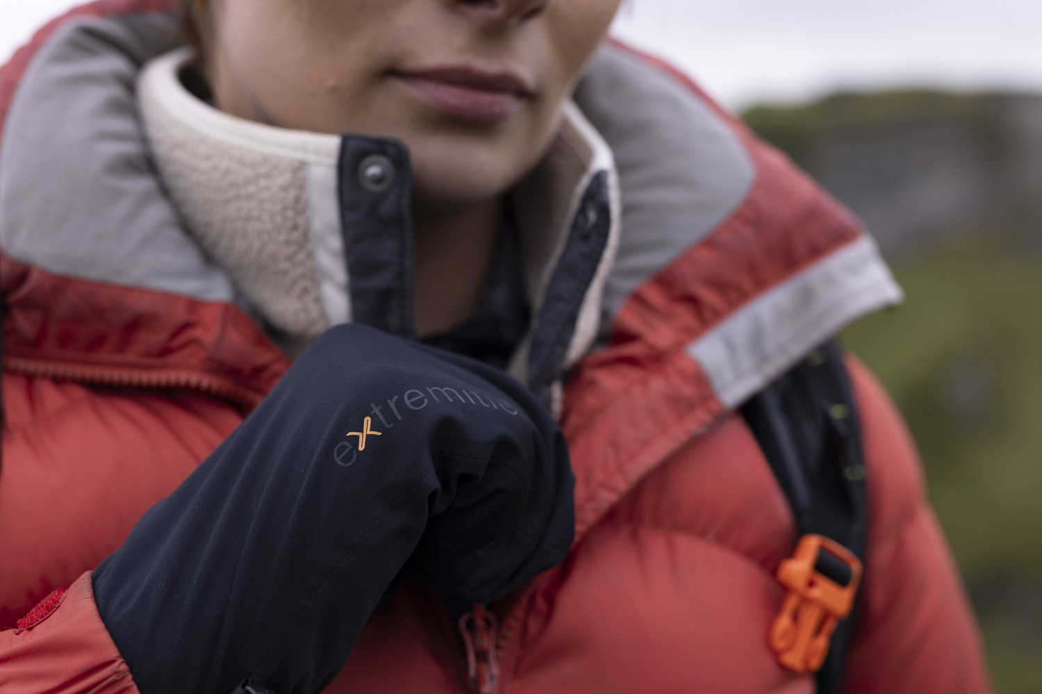 Close-up of a person wearing a red puffer jacket and a black glove, adjusting their collar outdoors, showcasing winter apparel and outdoor gear suitable for cold weather activities.