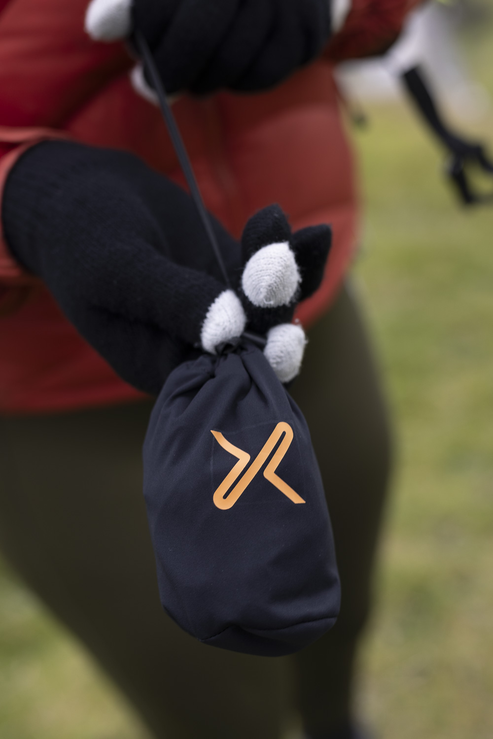 Person holding a compact, black pouch with an orange logo, featuring gloves designed for outdoor activities. The gloves have a unique design with white accents on the fingertips.
