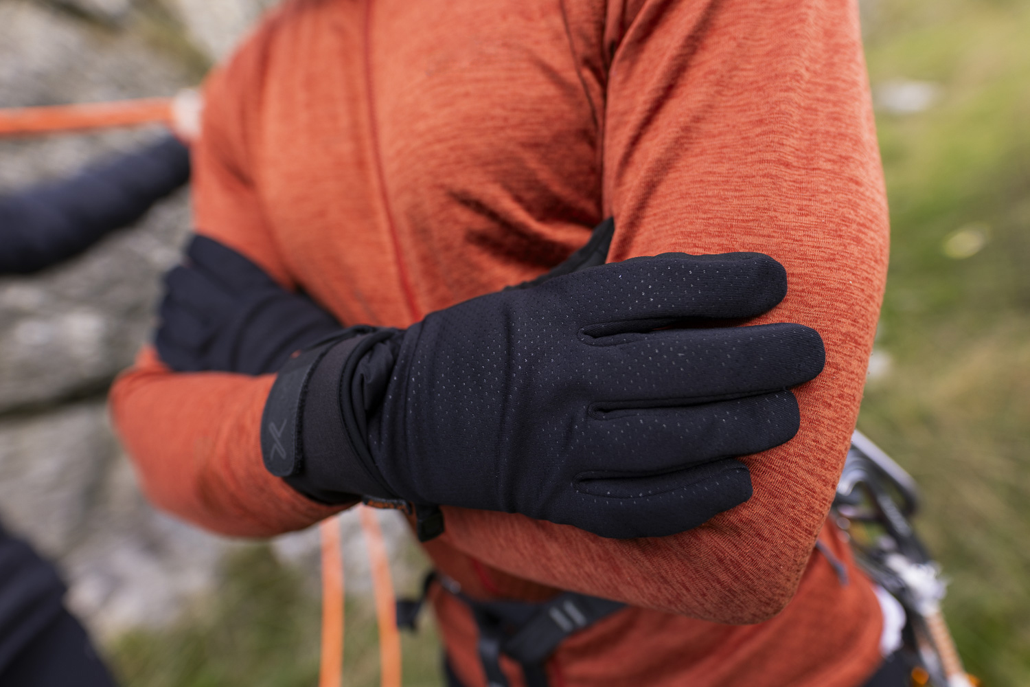 Close-up of a person wearing black gloves, with arms crossed, showcasing outdoor apparel in a rugged environment. Ideal for winter sports or climbing activities.