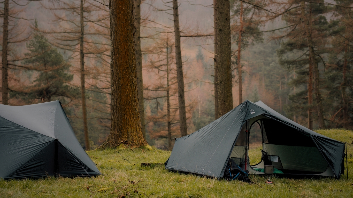 iO HP Banner 2 Two Terra Nova iO ultralight trekking pole tents pitched on a grassy forest clearing, showcasing their lightweight shelter design in a woodland setting.